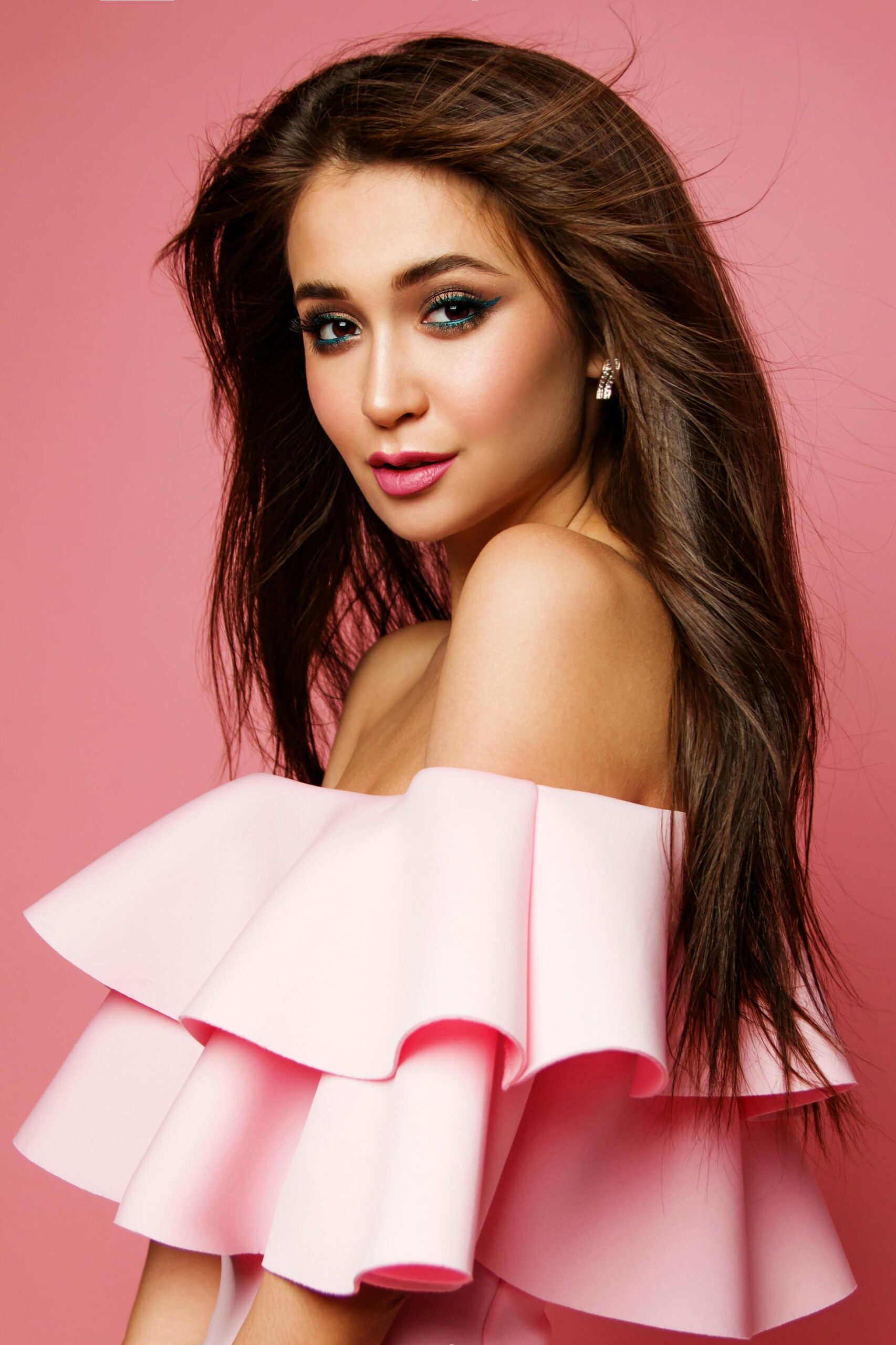 Chic portrait of a woman in a ruffled pink dress, showcasing stunning makeup and long hair.